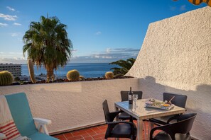 Eine Terrasse mit Esstisch, Stühlen, einem Kaktus und Blick auf den Ozean.