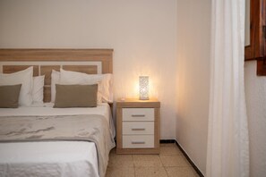 Un lit bien fait, avec une tête de lit, une table de chevet dotée de tiroirs et un luminaire fixé au mur.