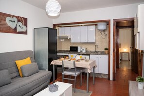 Un ambiente compatto con angolo cottura, zona pranzo e divano con cuscini.