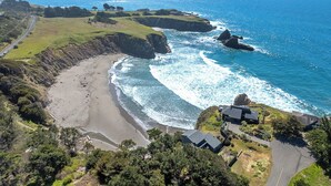 A coastal landscape with a beach, cliffs, and a road leading to a cluster of modern buildings. - The Redstone House at Mendocino Stone Ranch (Anchor Bay)