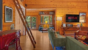 A wooden cabin interior with a living room, a staircase, a bookshelf, and a television. - The Redstone House at Mendocino Stone Ranch (Anchor Bay)
