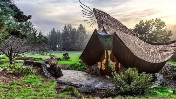 A modern, uniquely shaped building with a sloped roof and a large, curved entrance. - The Redstone House at Mendocino Stone Ranch (Anchor Bay)