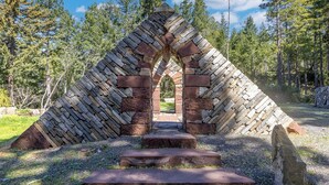 A stone archway with a pathway leading through it, surrounded by trees. - The Redstone House at Mendocino Stone Ranch (Anchor Bay)