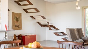 A dining area with a wooden table, chairs, and a bowl of fruit. There is a wall with geometric metal decorations and a hanging bag with text. - Villa Silvia with Swimming Pool by Wonderful Italy (Noto)