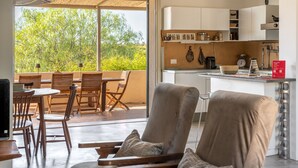 A modern kitchen with white cabinets, a dining area with wooden furniture, and a large window overlooking greenery. - Villa Silvia with Swimming Pool by Wonderful Italy (Noto)