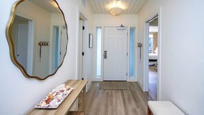 Un pasillo con un banco de madera, un espejo grande y una puerta que da a un dormitorio.