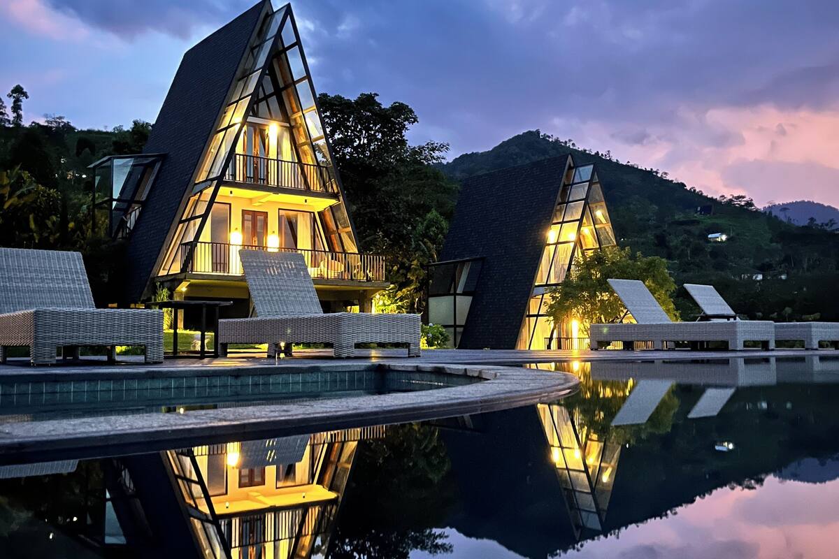 A modern hotel with a unique triangular architecture, featuring a pool and outdoor seating areas.