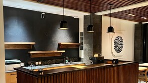 Eine moderne Küche mit Kochinsel, Holzvertäfelung, Pendelleuchten und einer schwarzen Spritzschutzwand.