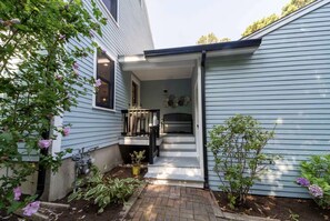 A house with a covered porch, a small garden, and a visible window. - Welcome to Plaisir d’Amour — “The Pleasure of Love”!  Sleeping 10! (Dennis)