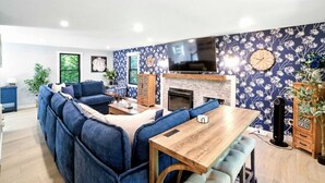 Ein Wohnzimmer mit Ecksofa, Esstisch aus Holz, Kamin und an der Wand befestigtem Fernseher.