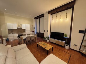 Een moderne woonkamer met een bank, een salontafel en een televisie. Er is een keuken met kastjes en een eettafel.