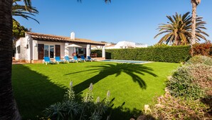 Ein Haus mit Schwimmbad, blauen Liegestühlen und einem gepflegten Rasen.