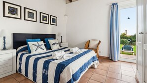 Ein Schlafzimmer mit Bett, Sessel, Nachttisch, Lampe und Blick ins Freie.