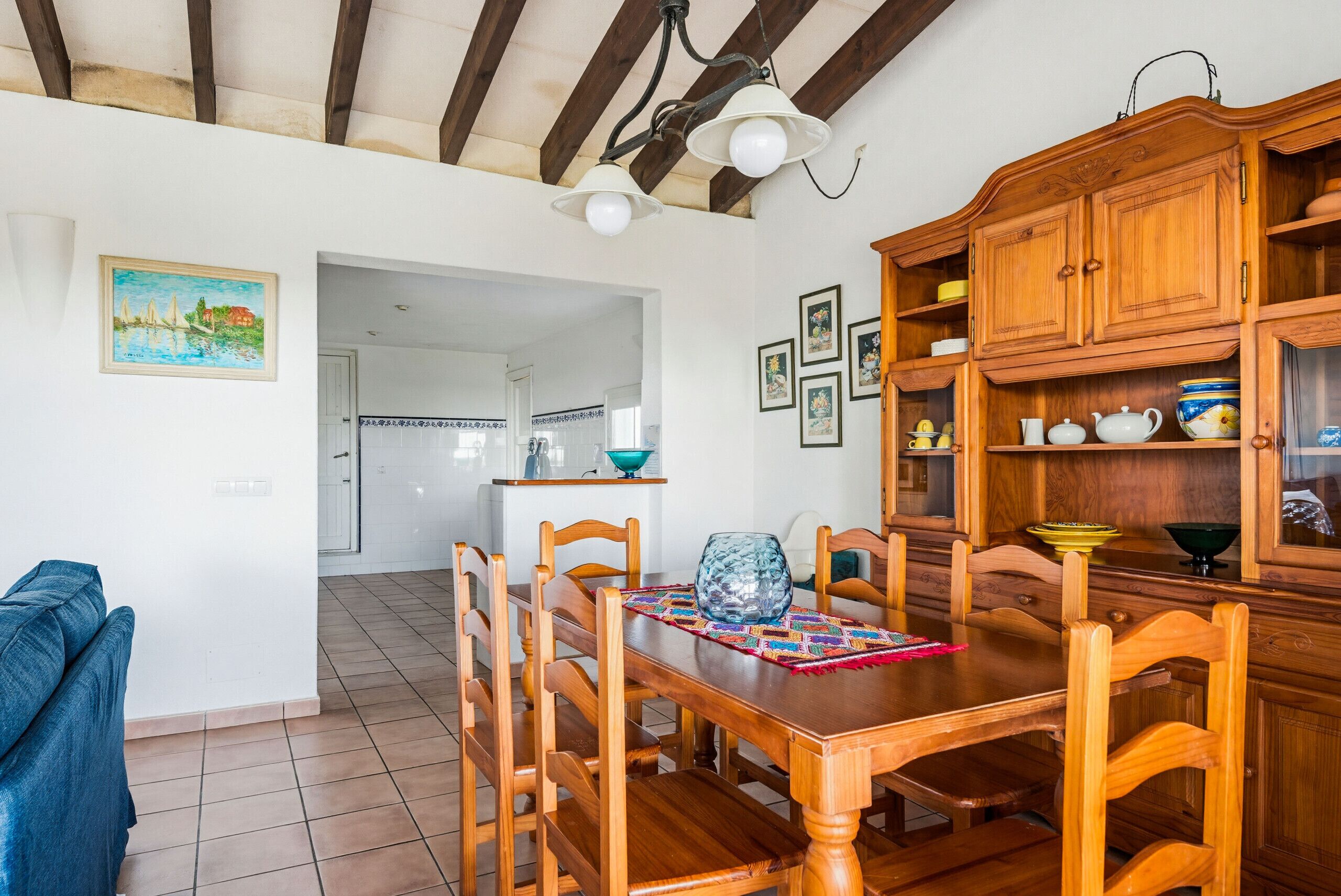 A dining area with wooden furniture, a tiled floor, and a kitchen in the background.