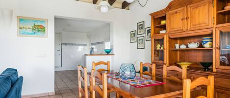A dining area with wooden furniture, a tiled floor, and a kitchen in the background.