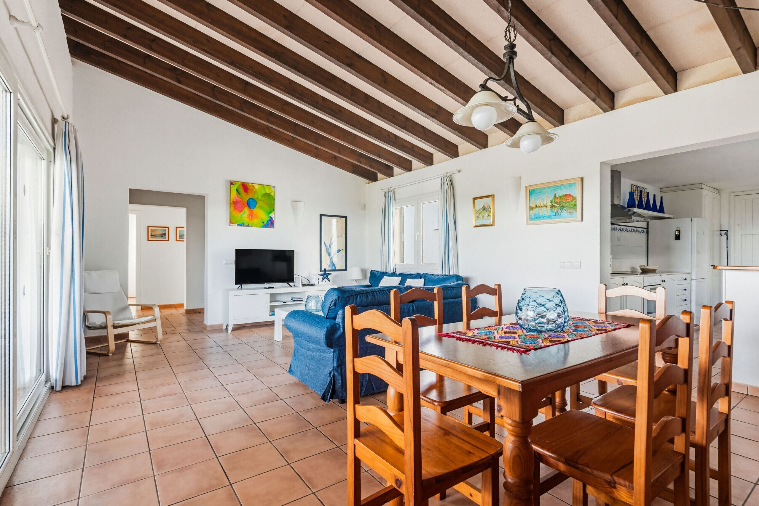 Uma sala de estar espaçosa com uma mesa de jantar de madeira, sofá azul e televisão.