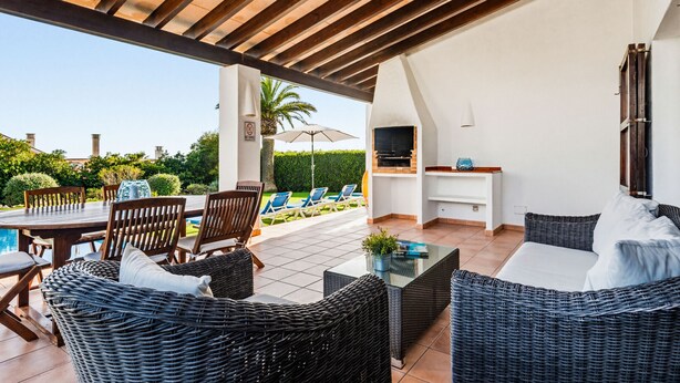 Eine Terrasse im Freien mit Korbmöbeln, einem Pool und einem Fernseher.