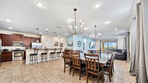 A spacious kitchen with modern appliances, a dining area with wooden chairs, and a large chandelier. - Pool Table, Arcade, Foosball, Resort-style Pool: Sunny Villa (Kissimmee)