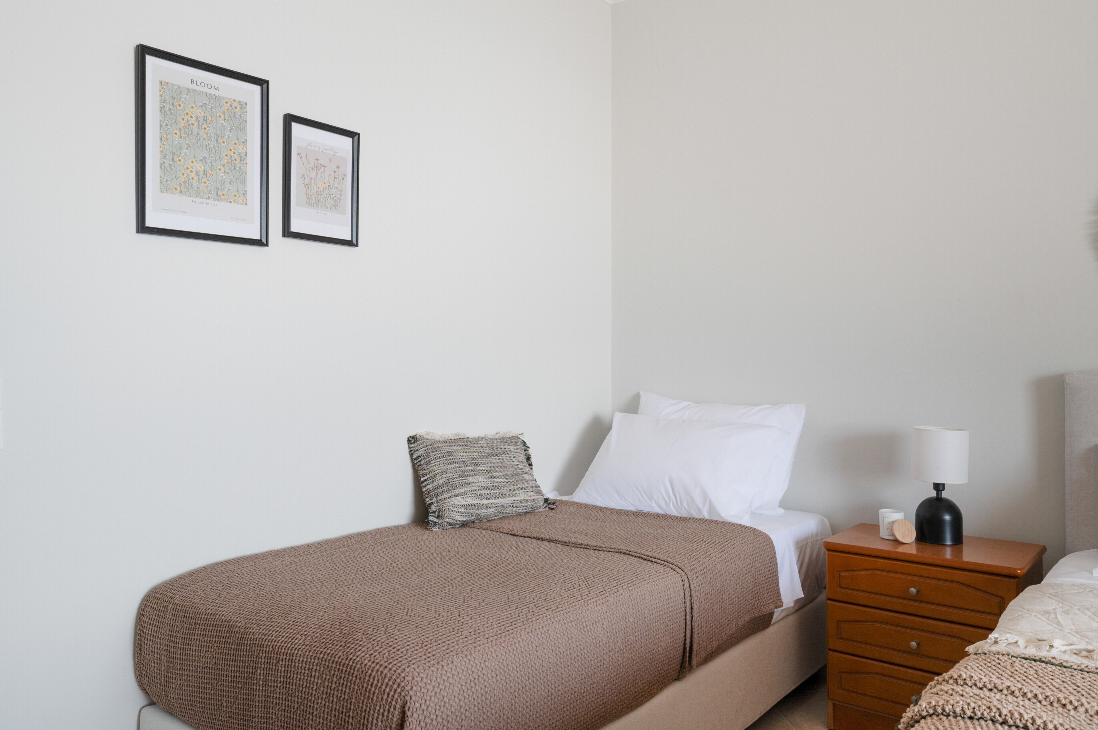 A bedroom with a bed, a nightstand, a lamp, and two framed pictures on the wall.