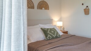 Un letto rifatto con biancheria bianca e marrone, un cuscino verde e una lampada da comodino.