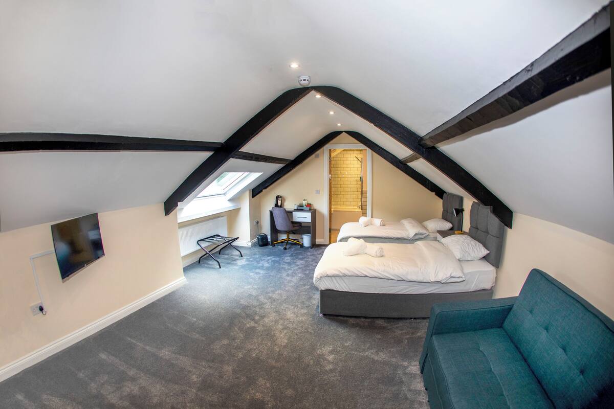 A bedroom with a sloped ceiling, a bed, a sofa, a desk, and a chair.