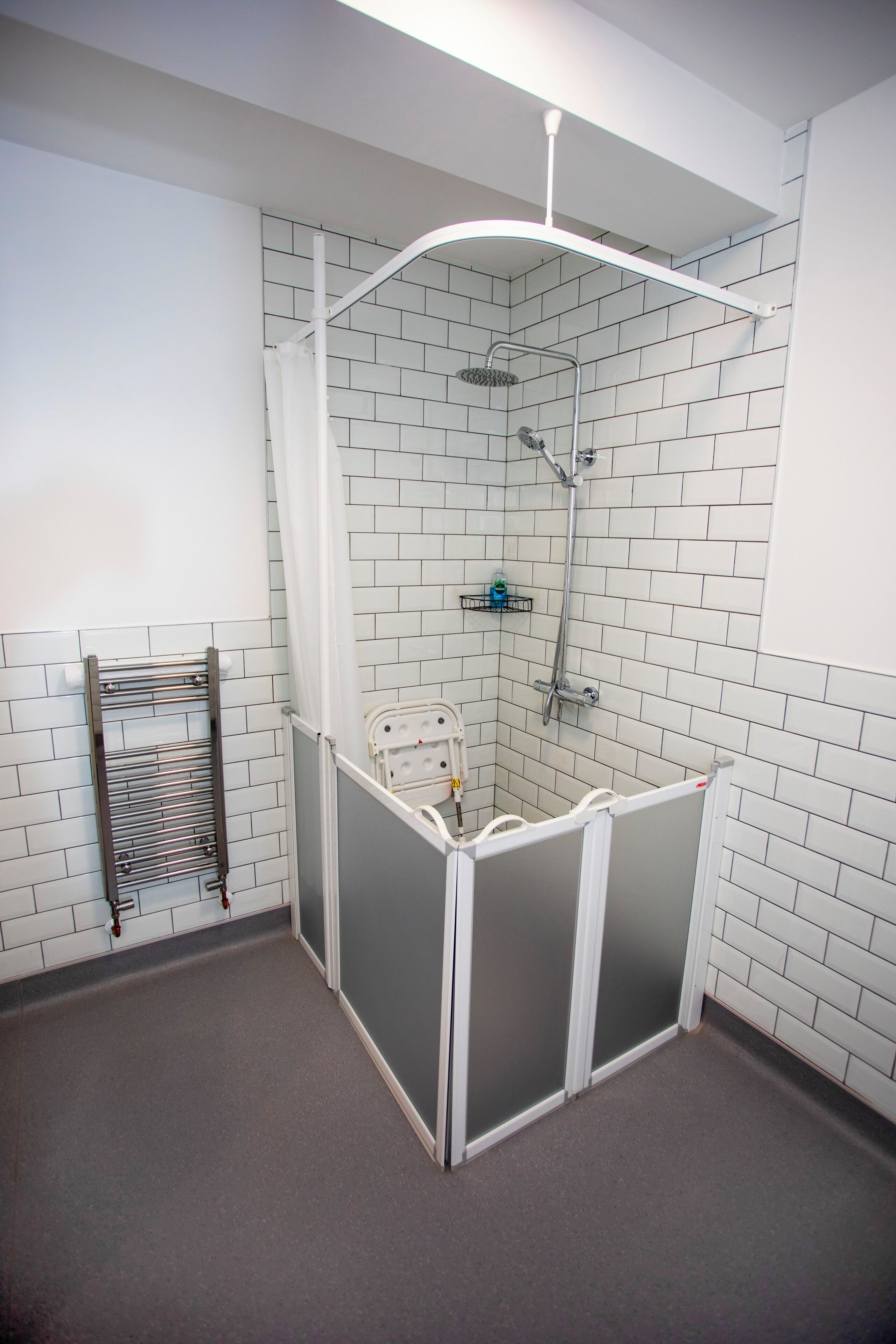 Un petit espace douche fermé, doté d’un pommeau de douche blanc fixé au mur, d’un pommeau de douche à main et d’une cabine de douche en verre.