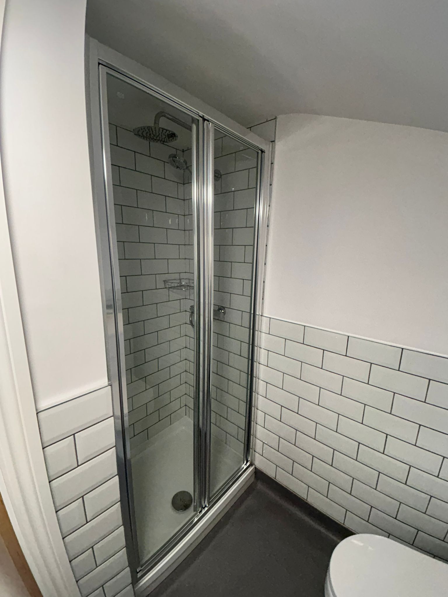 A small, modern bathroom with a glass-enclosed shower, white subway tiles, and a white toilet.