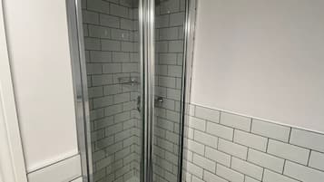 A small, modern bathroom with a glass-enclosed shower, white subway tiles, and a white toilet.