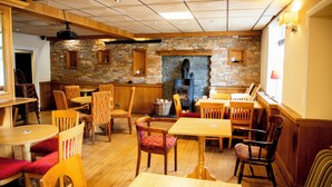 A cozy restaurant with wooden tables and chairs, a stone wall, and a fireplace. - Cresselly Inn (Mountain Ash)