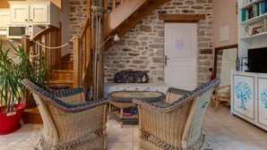 Una sala de estar acogedora con mobiliario de mimbre, una pared de piedra, una escalera de madera y un televisor sobre un mueble.