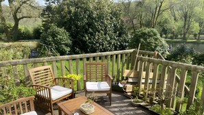 Una terraza de madera con una mesa y sillas, rodeada de plantas en macetas y vistas al río.