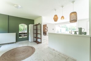 Cozinha moderna com bancada branca, luminárias de vime suspensas e vista para o exterior.