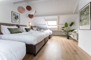Quarto com uma cama grande, uma cama menor, uma janela, uma planta e obras de arte nas paredes.