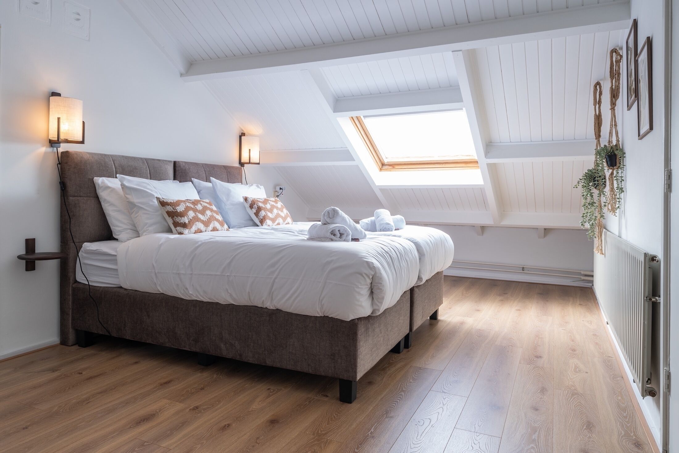 A bedroom with a bed, two wall-mounted lights, a skylight, and a radiator.