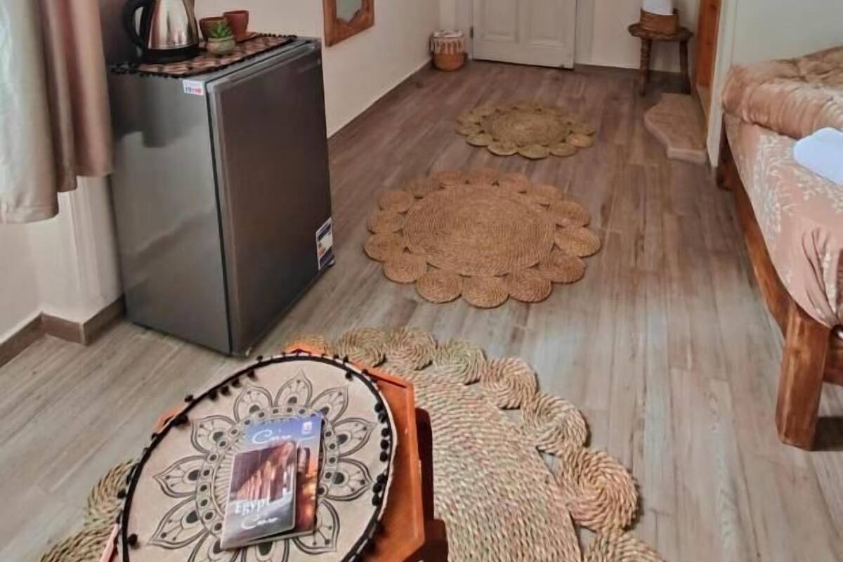 A compact living space with a refrigerator, a wooden shelf, a door, and a bed.