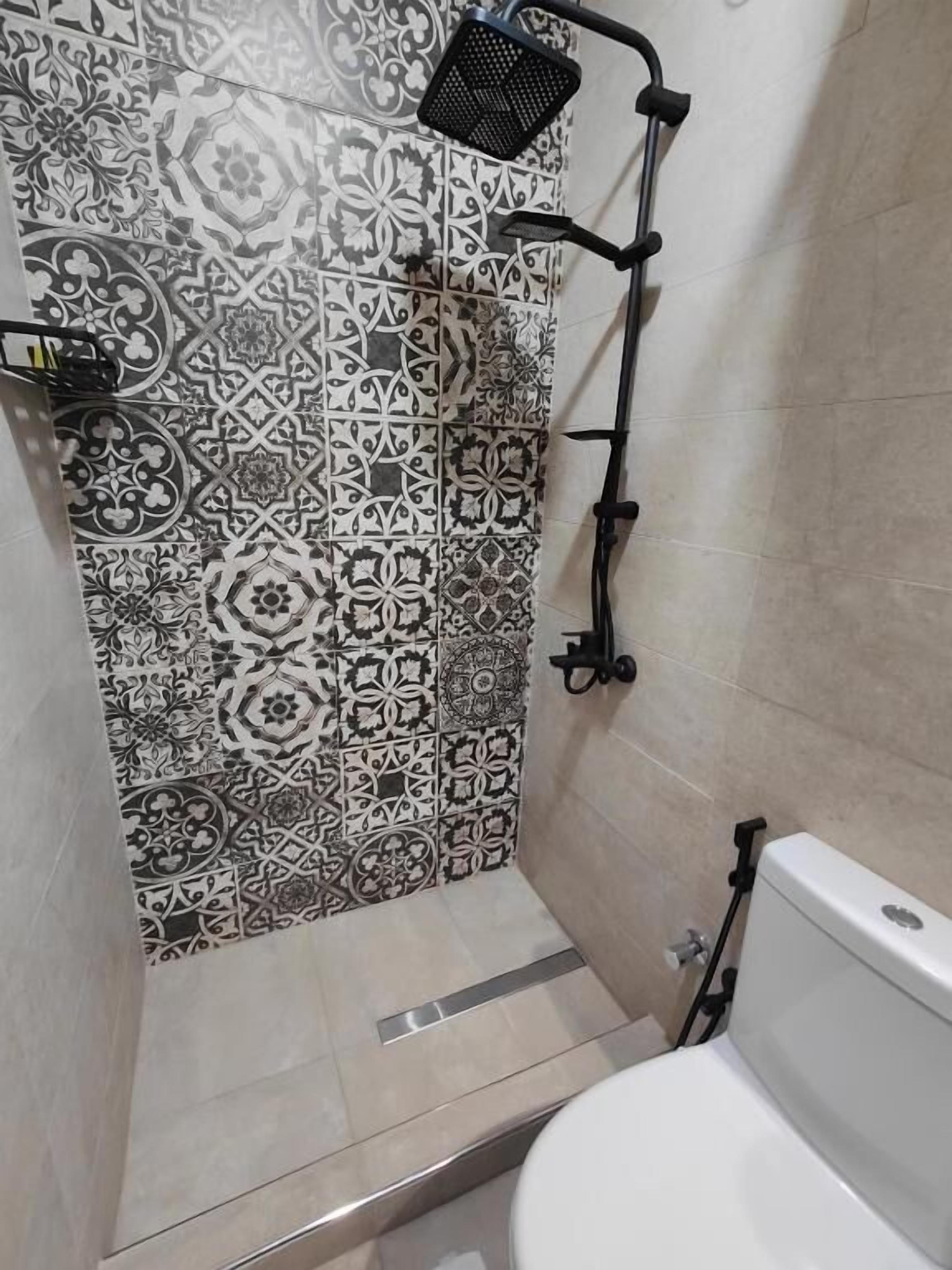 A bathroom with a shower area featuring patterned tiles, a toilet, and a handheld showerhead.