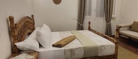 A bedroom with a wooden bed, a bedside table, a large rug, and a window with curtains.