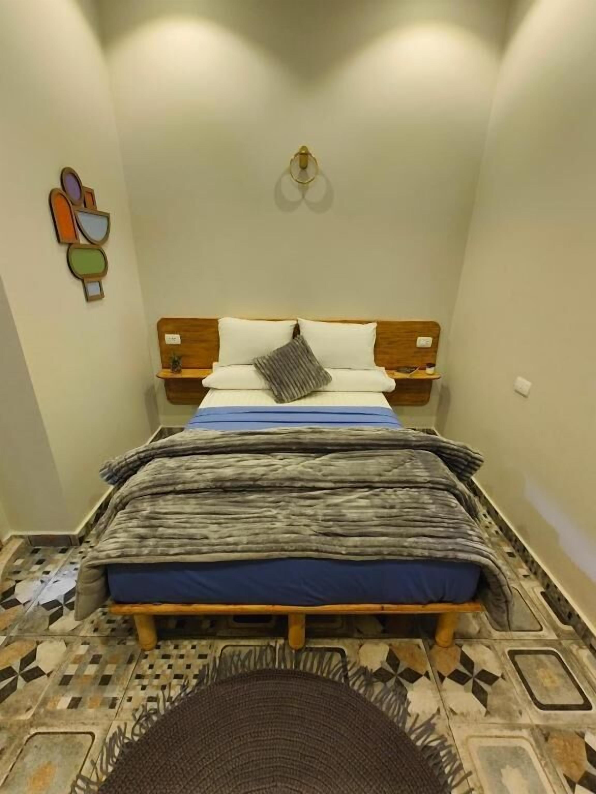 A small, cozy room with a bed, a nightstand, and a wall-mounted light fixture.