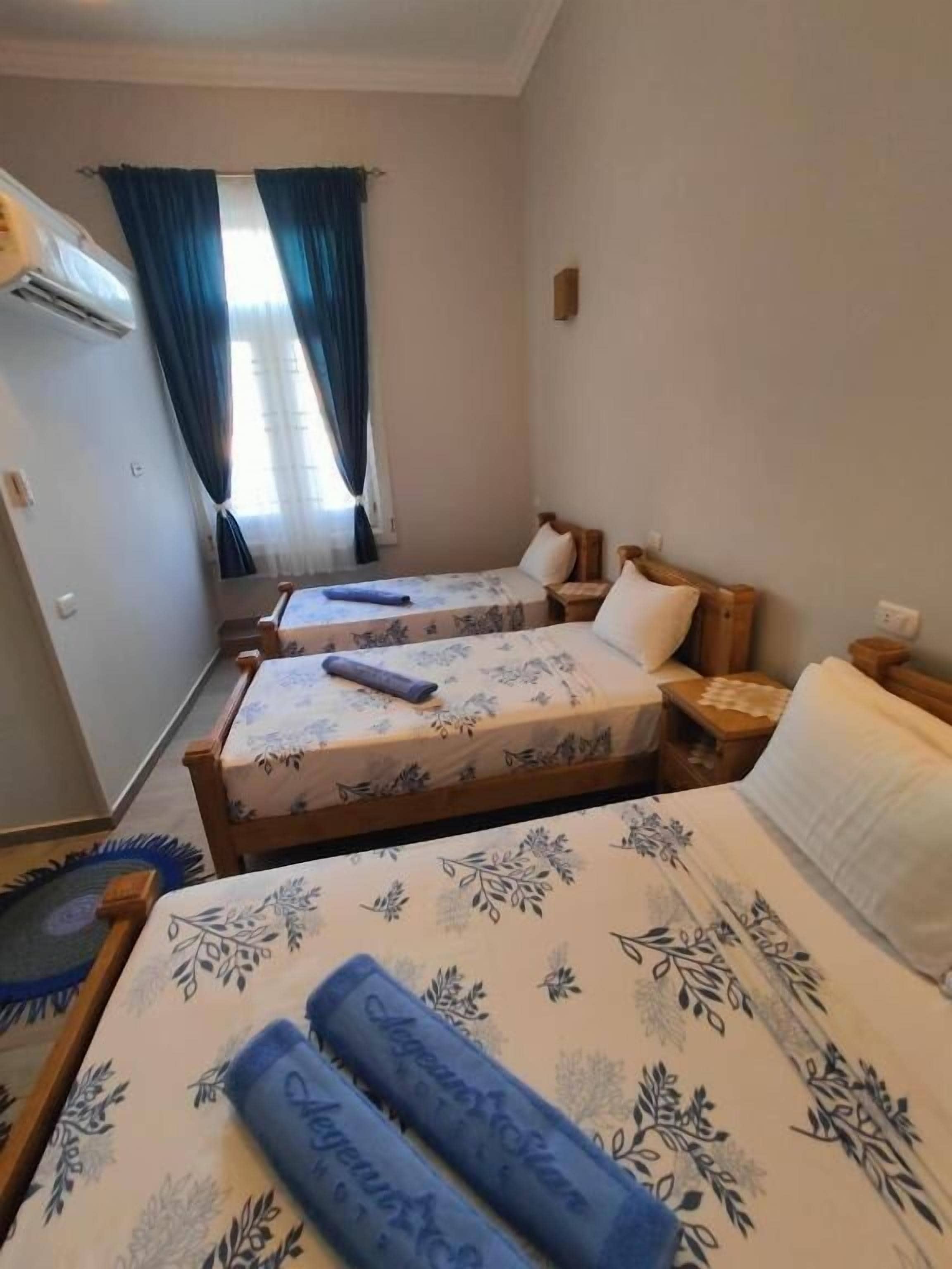 Quarto de hotel com duas camas, uma cama de casal com toalhas enroladas e uma cama menor com um travesseiro.