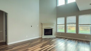 Amplia habitación con suelo de madera, chimenea, ventanas grandes y una puerta que da a otra estancia.
