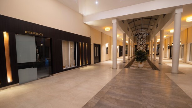 A modern hotel lobby with a restaurant on the left, a central column with a decorative pattern, and a spacious, well-lit corridor. - D'WAYFARER INN Resort  (Erode)