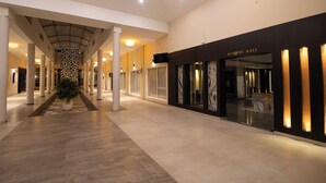 A spacious corridor with a modern design, featuring a central column with a decorative pattern, a potted plant, and a restaurant named "BANQUET HALL" on the right. - D'WAYFARER INN Resort  (Erode)