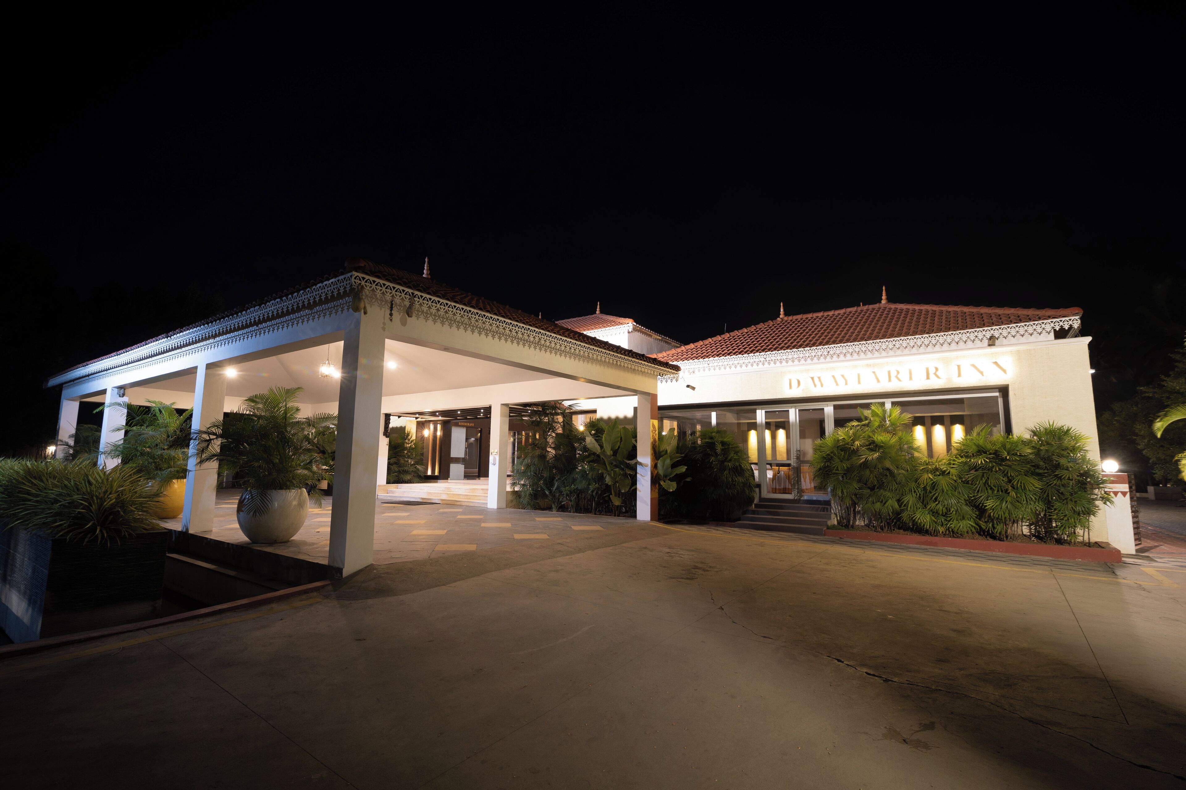 A hotel entrance with a covered walkway, potted plants, and a tiled roof.