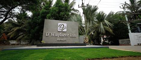 A sign for D'Wayfarer Inn Resort with a logo, surrounded by greenery and palm trees.