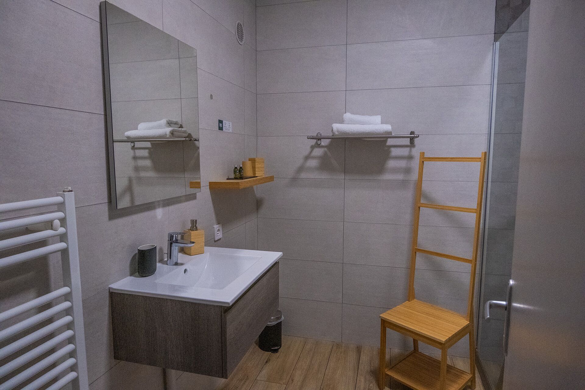 Un baño pequeño con lavamanos, espejo, toallero y estante de madera.