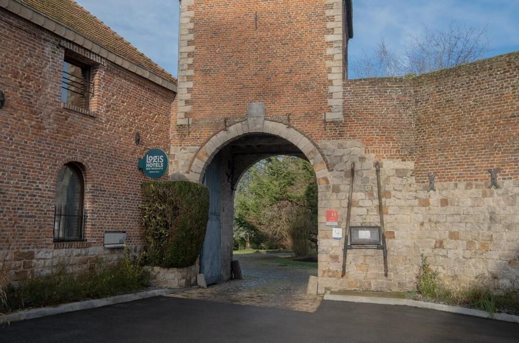 Un edificio de ladrillo con un arco de piedra en la entrada, un cartel de Logis Hotels y una pequeña placa en la pared.