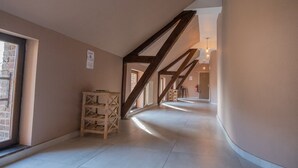 Un pasillo con vigas de madera a la vista, una estantería de madera y un extintor.