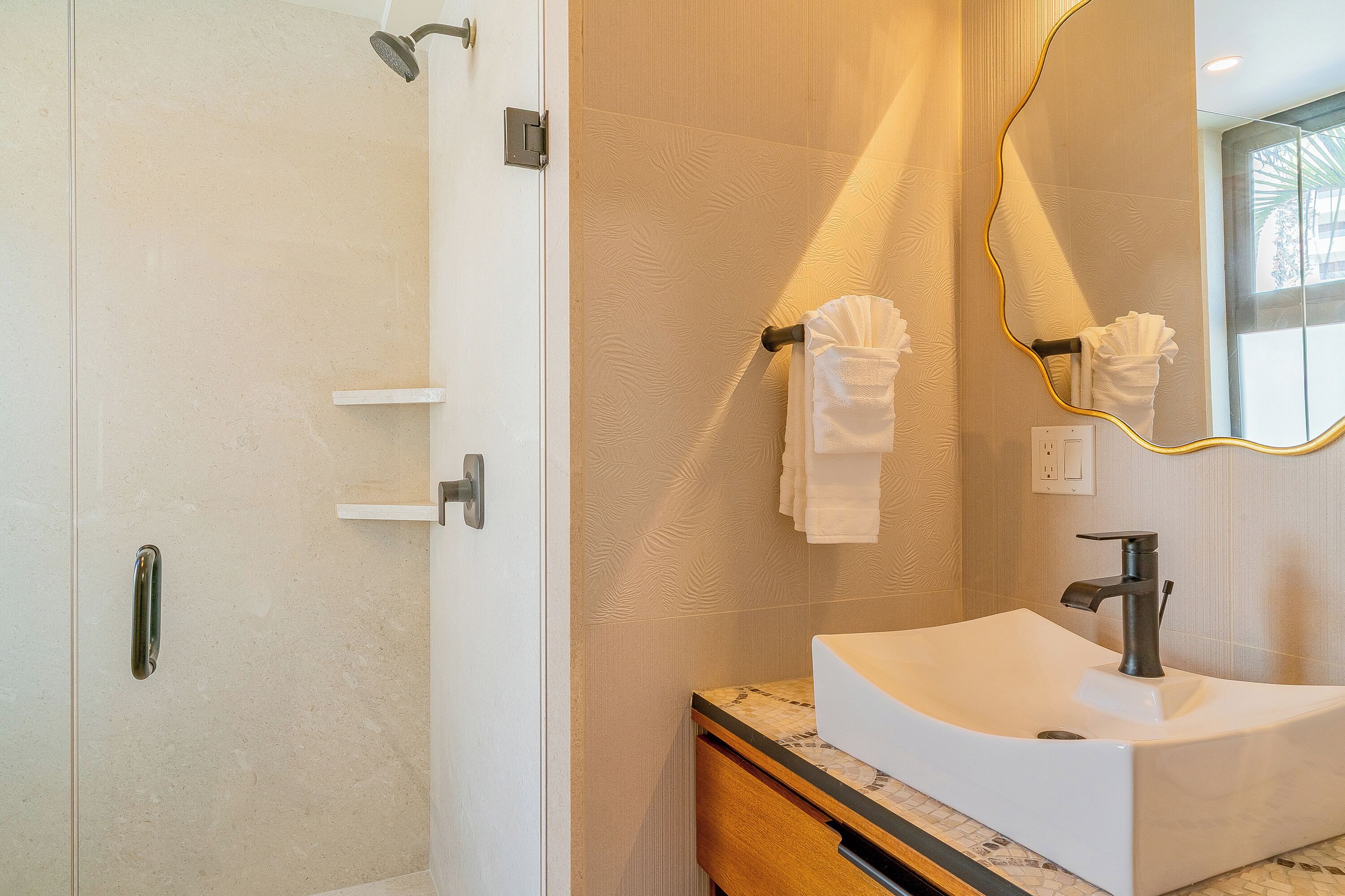 Ein modernes Badezimmer mit Dusche, Waschtisch und einem Spiegel mit goldener Rahmung.