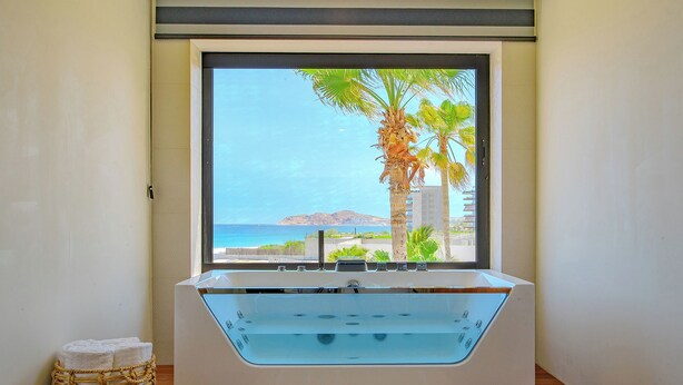 Um banheiro moderno com uma banheira grande, vista para o oceano e uma cesta de vime com toalhas.