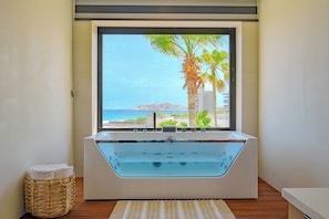 Ein modernes Badezimmer mit einer großen Badewanne, Meerblick und einem Korbwäscheschrank mit Handtüchern.